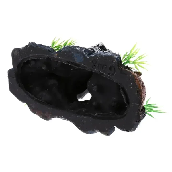 Crâne résine sur base rocheuse noire avec os et plantes artificielles vertes.